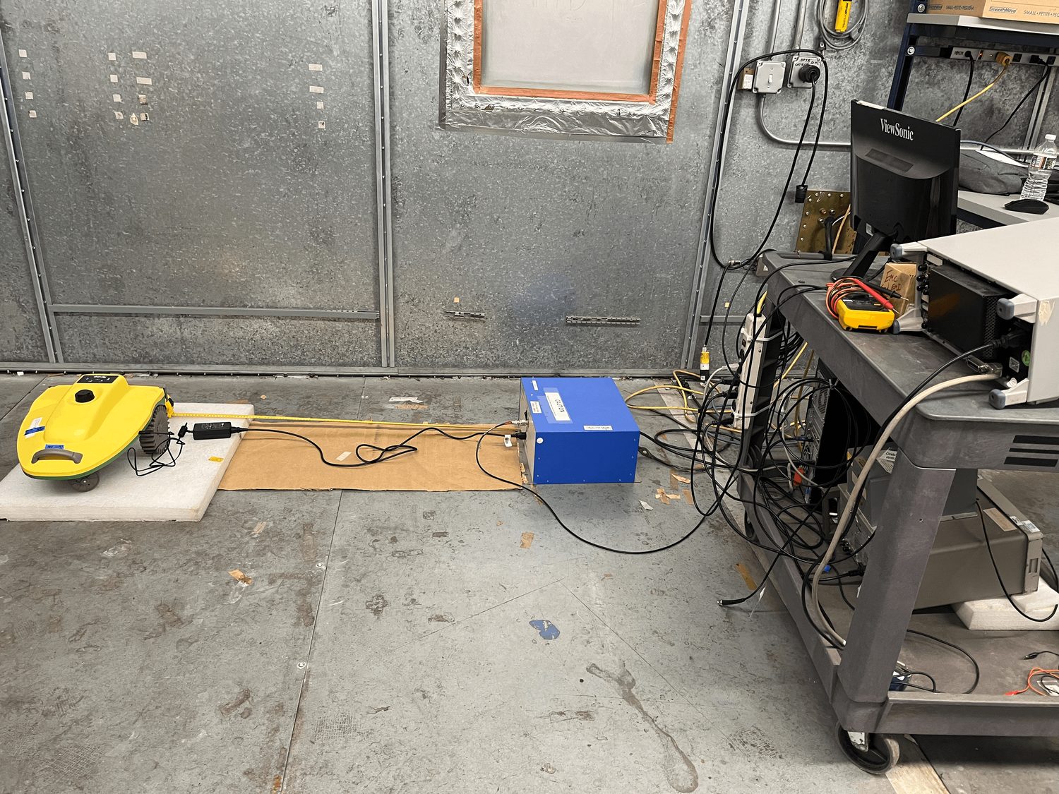 EMC pre-compliance test setup with a robotics device on a ground plane, cabled to test equipment in a shielded room