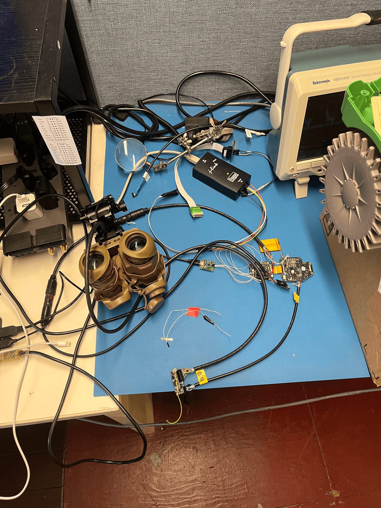 Night vision goggle housing on a workbench connected to debug probes and an oscilloscope during bring-up