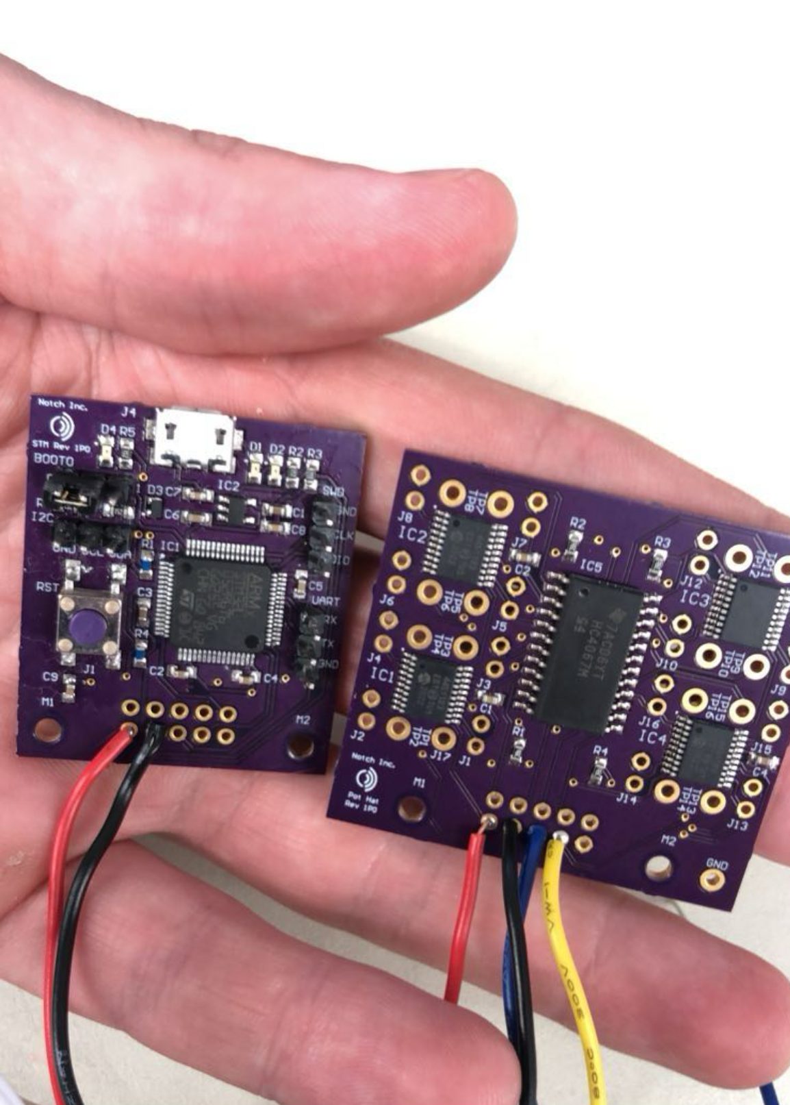 The two-board stack held in a hand for scale, with power and signal wires connected